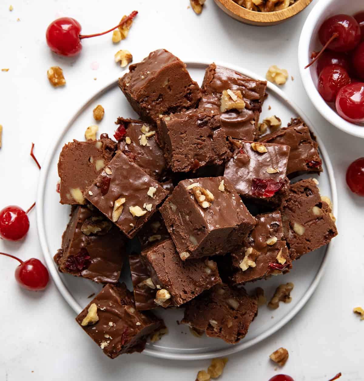 Plate of Cherry Fantasy Fudge cut into pieces with cherries next to it from overhead.