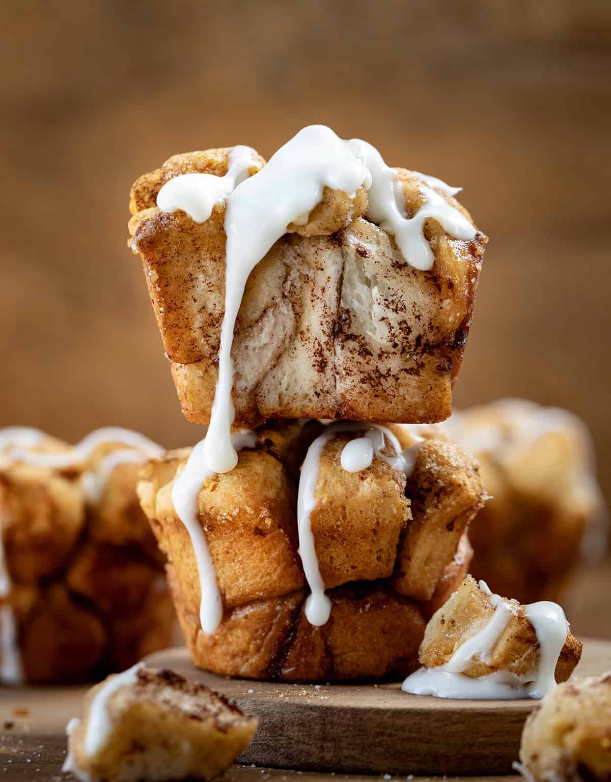 Stacked Cinnamon Roll Monkey Bread Muffins on a wooden table with vanilla glaze dripping down muffins.