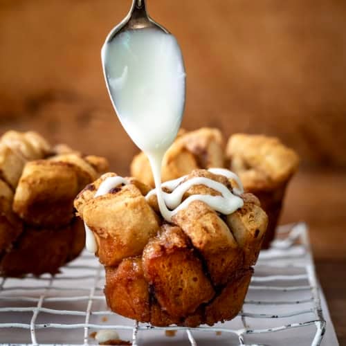 Drizzling glaze over Cinnamon Roll Monkey Bread Muffins.