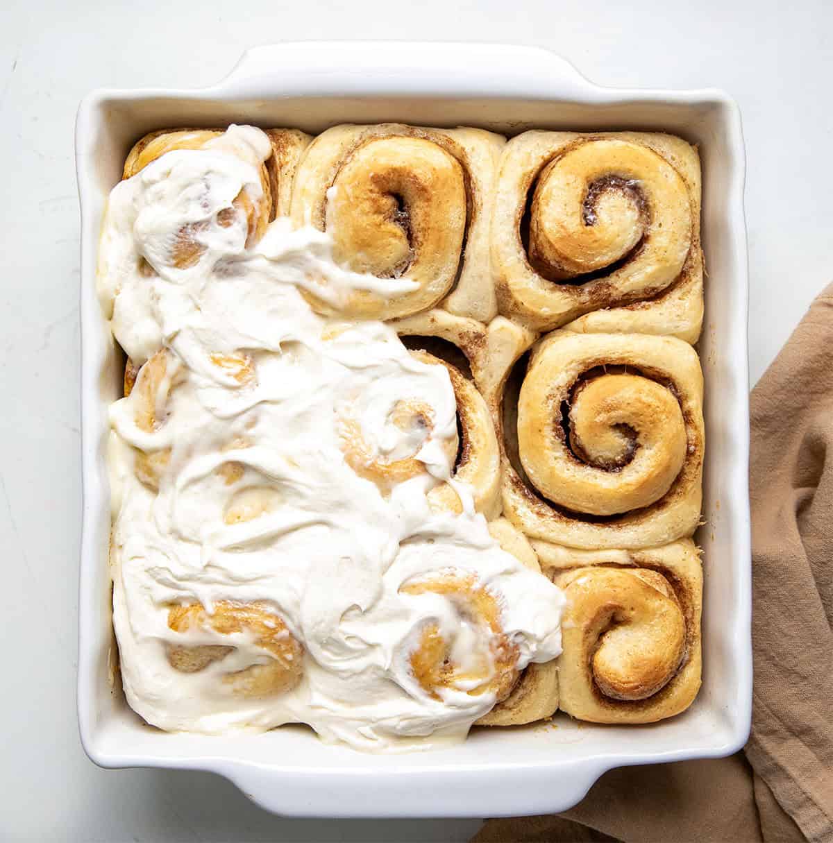 Pan of One Hour Cinnamon Rolls with half of the frosting spread over the rolls on a white table from overhead.