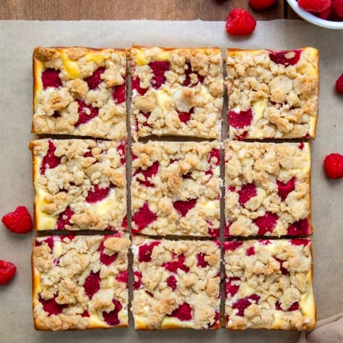 Raspberry Cheesecake Bars cut into squares on a wooden table with fresh raspberries.