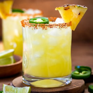 Close up of glasses of Spicy Pineapple Margarita on a wooden table.