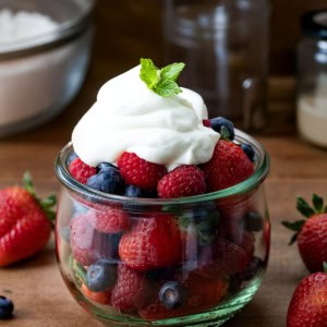 Whipped Cream Cheese Frosting dolloped on a jar of fresh fruit on a wooden table.