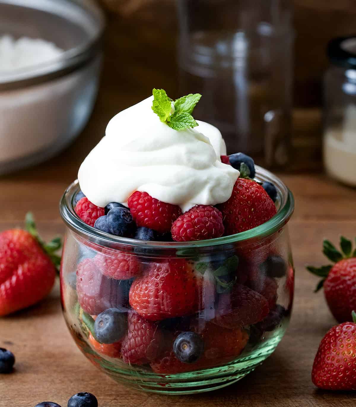 Whipped Cream Cheese Frosting dolloped on a jar of fresh fruit on a wooden table.