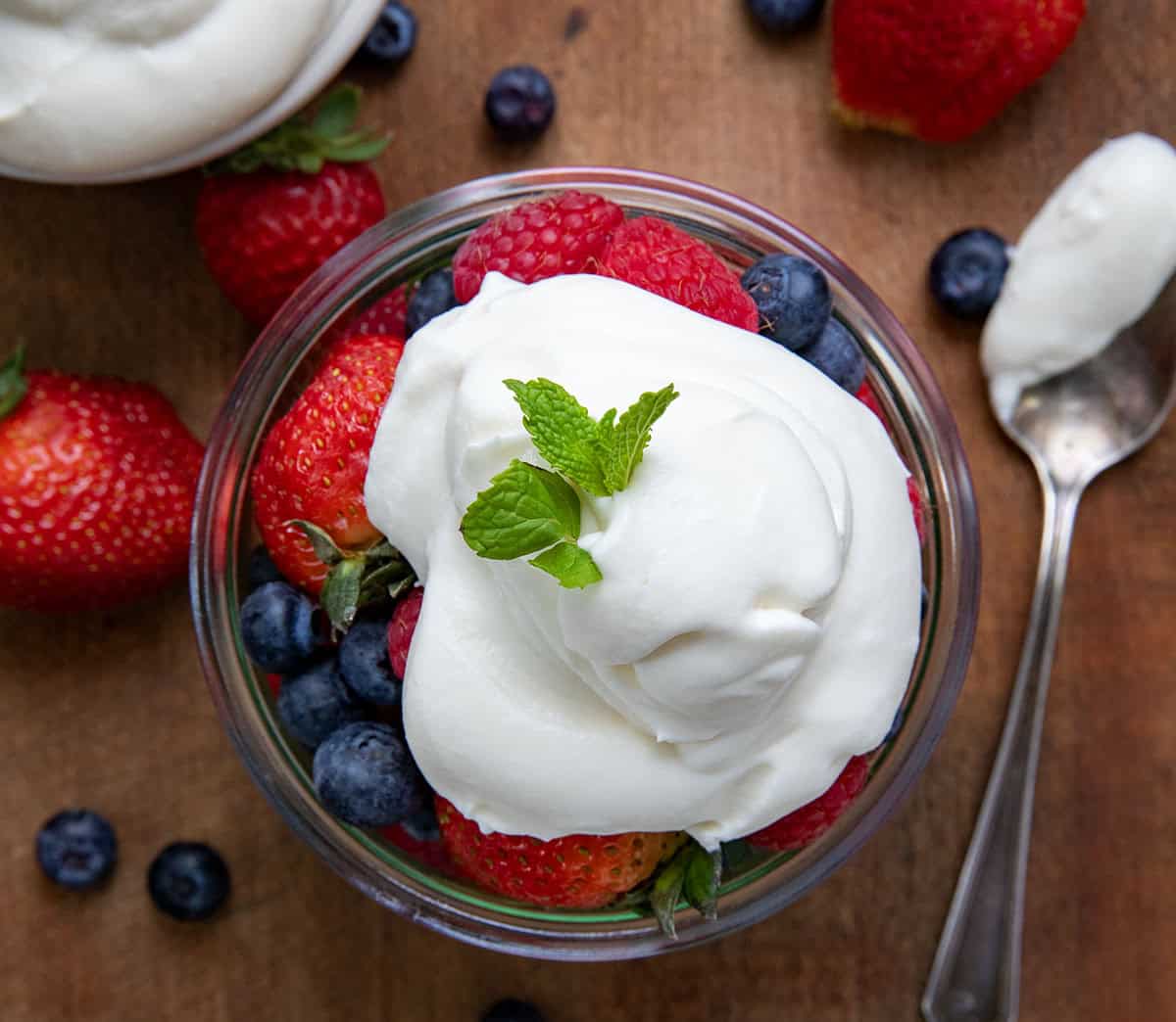 Whipped Cream Cheese Frosting on top of a jar of fruit on a wooden table from overhead.