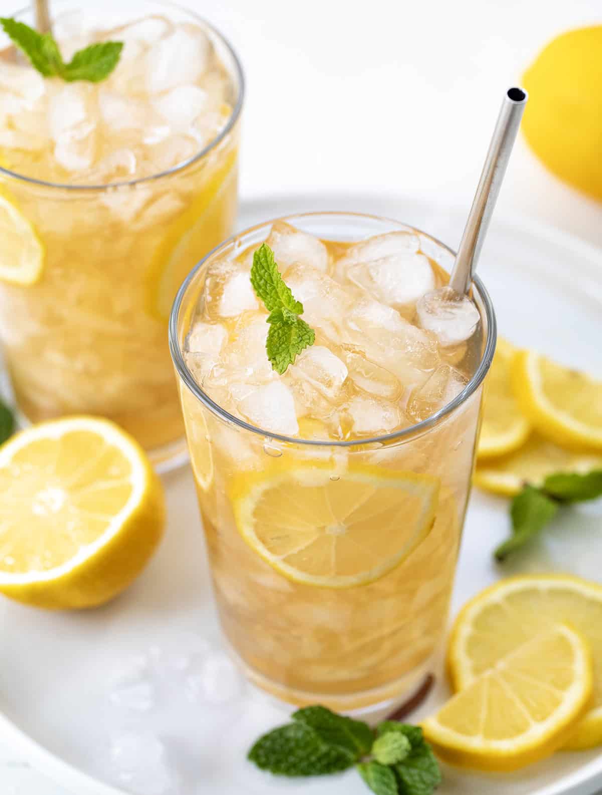 Glasses of Arnold Palmer on a white tray with fresh lemon and mint.