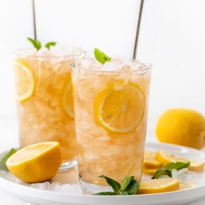 Glasses of Arnold Palmer on a white tray with fresh lemon, ice, and mint.