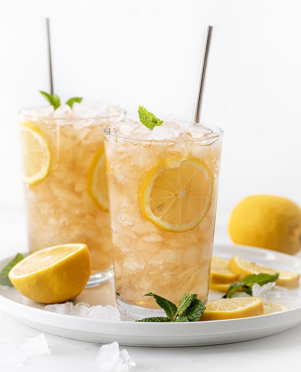 Glasses of Arnold Palmer on a white tray with fresh lemon, ice, and mint.