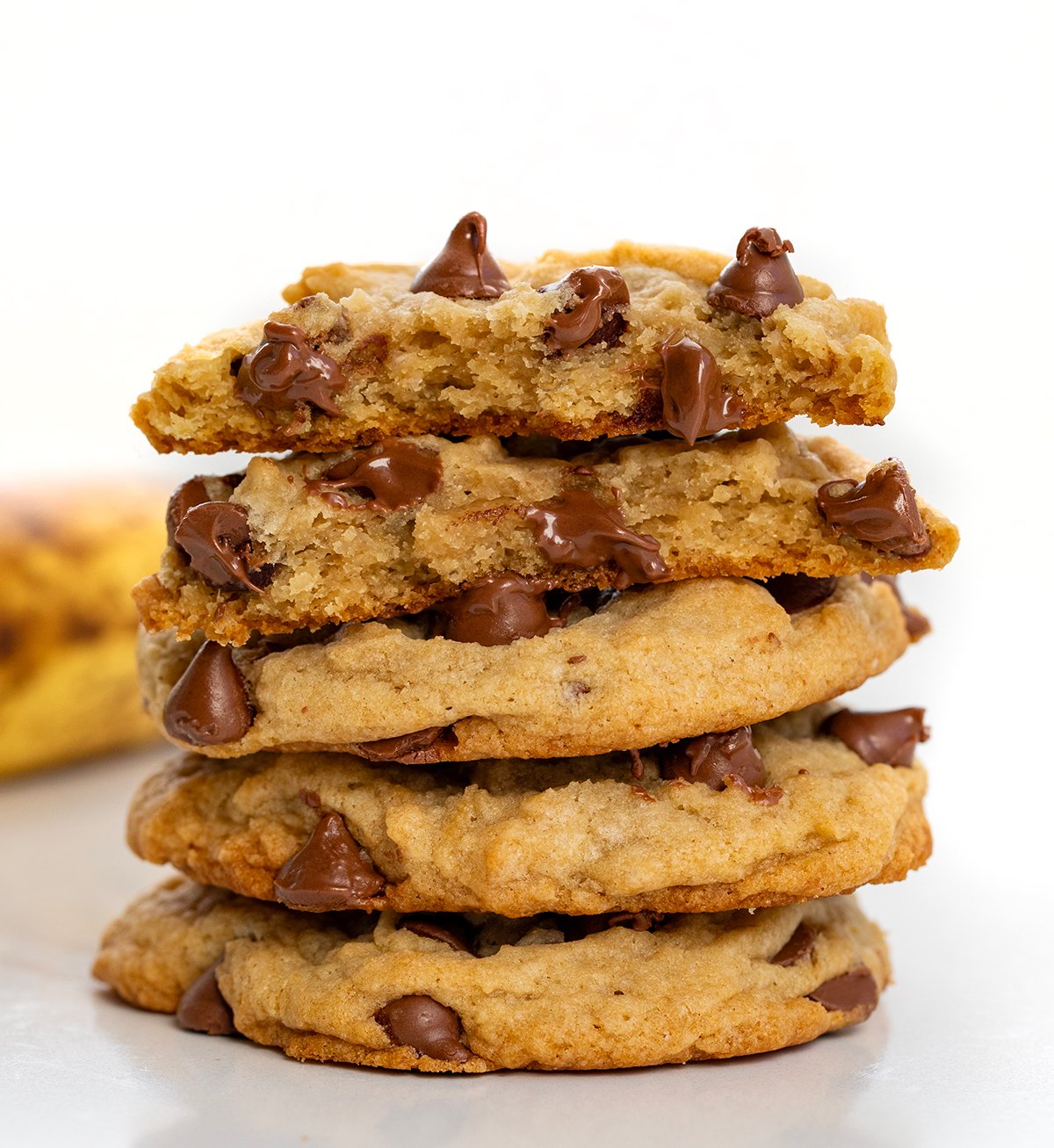 Stack of Chewy Banana Chocolate Chip Cookies with top cookie broken in half showing gooey chocolate chips.