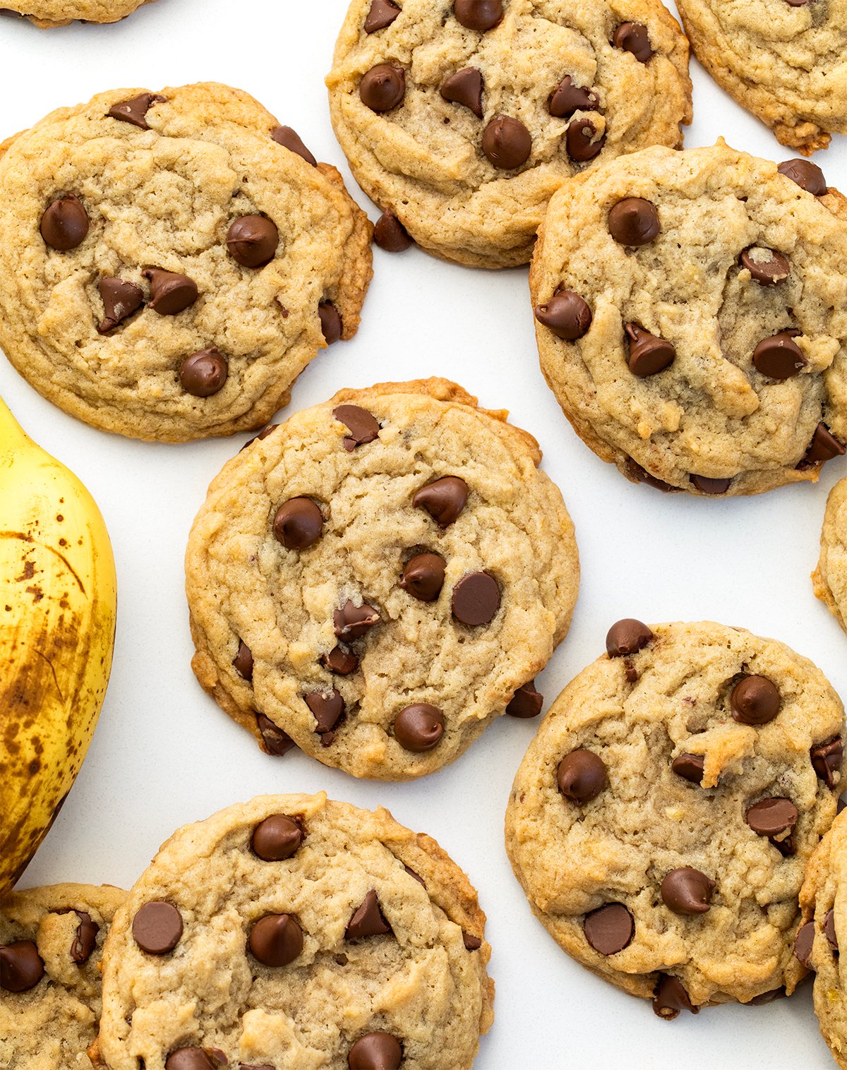 Chewy Banana Chocolate Chip Cookies on a white table with a banana from overhead.