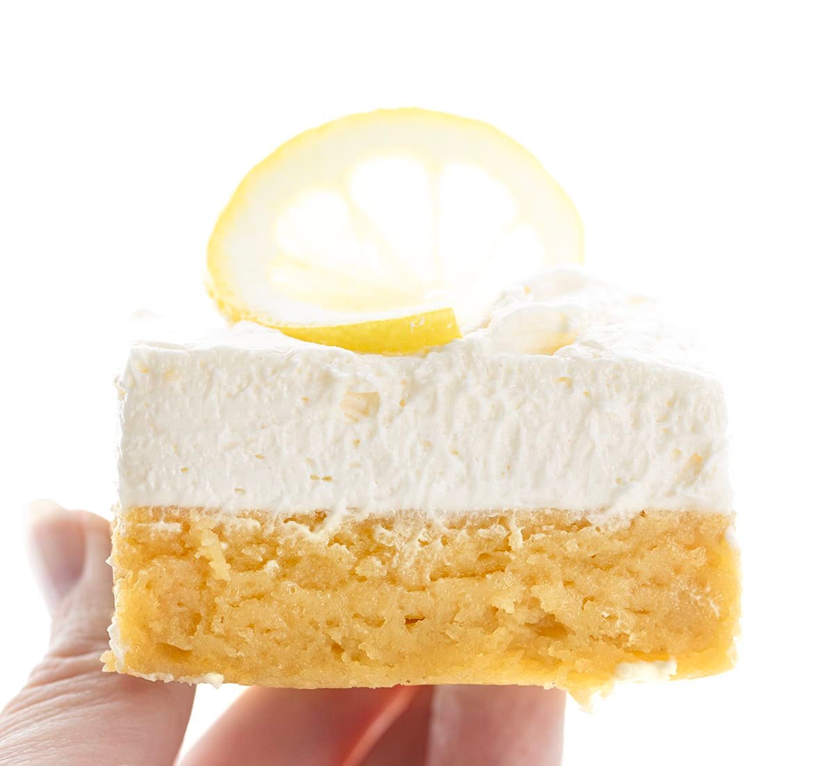 Hand holding a Frosted Lemon Brownie with fresh lemon on top.