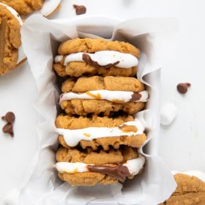 Basket of Peanut Butter S'mores Sandwich Cookies on a white table with cookies surrounding it from overhead.