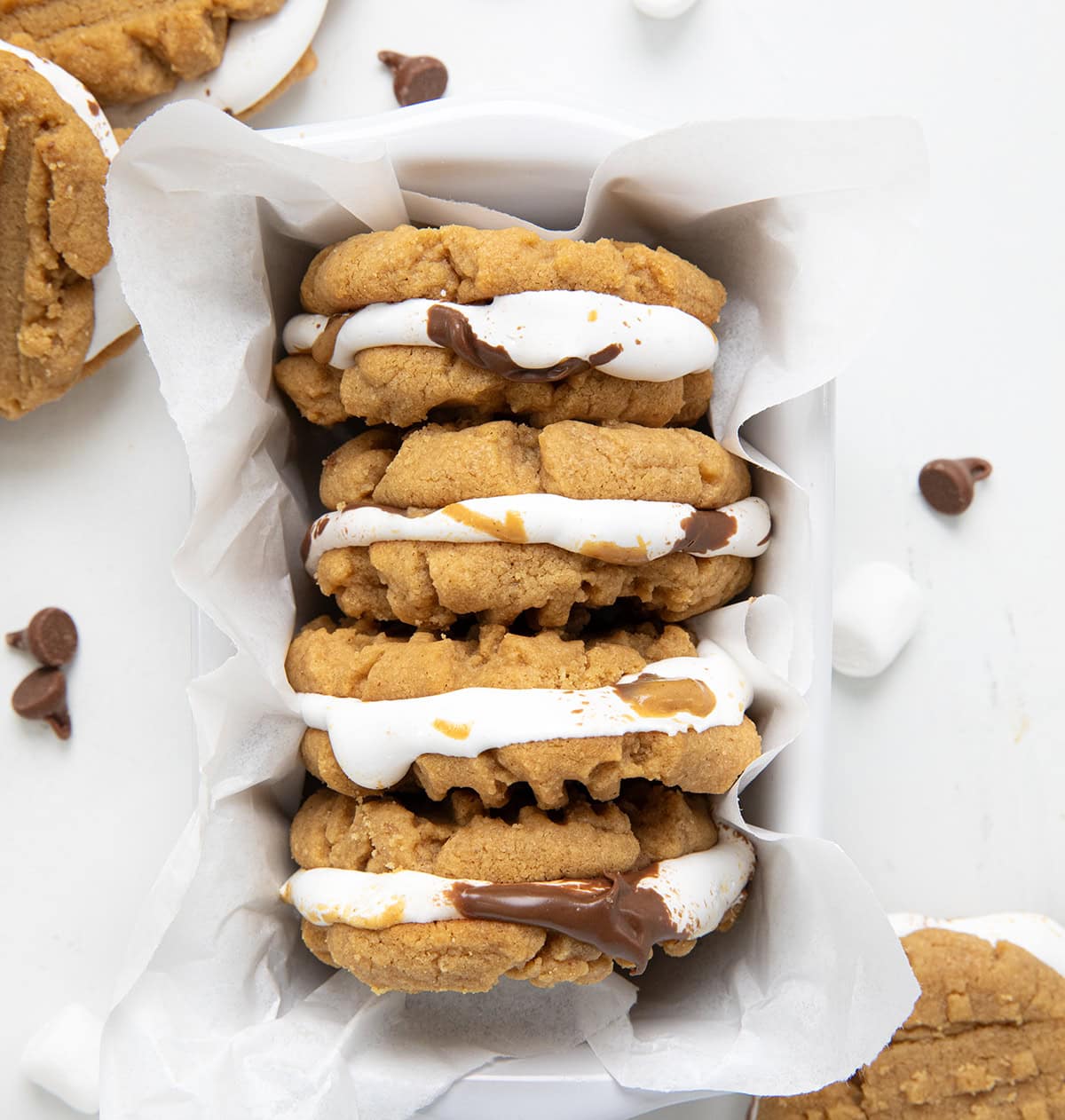 Basket of Peanut Butter S'mores Sandwich Cookies on a white table with cookies surrounding it from overhead.