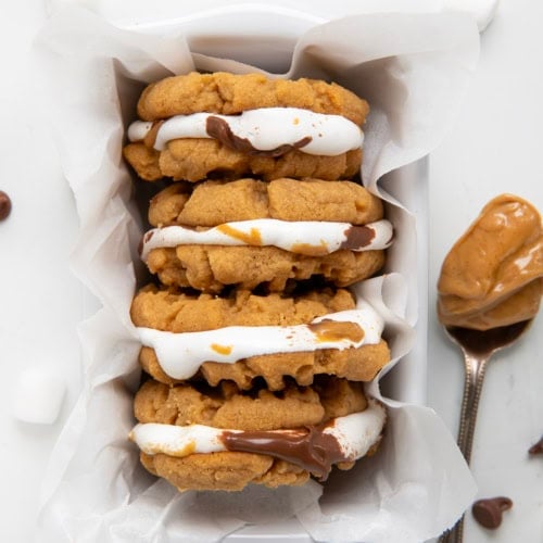 Peanut Butter S'mores Sandwich Cookies in a basket with a spoonful of peanut butter on the white table.