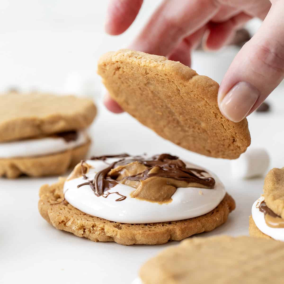 Assembling a Peanut Butter S'mores Sandwich Cookie with a hand setting down the top cookie.