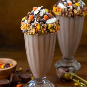 Two Ultimate Peanut Butter Chocolate Milkshakes on a wooden table.