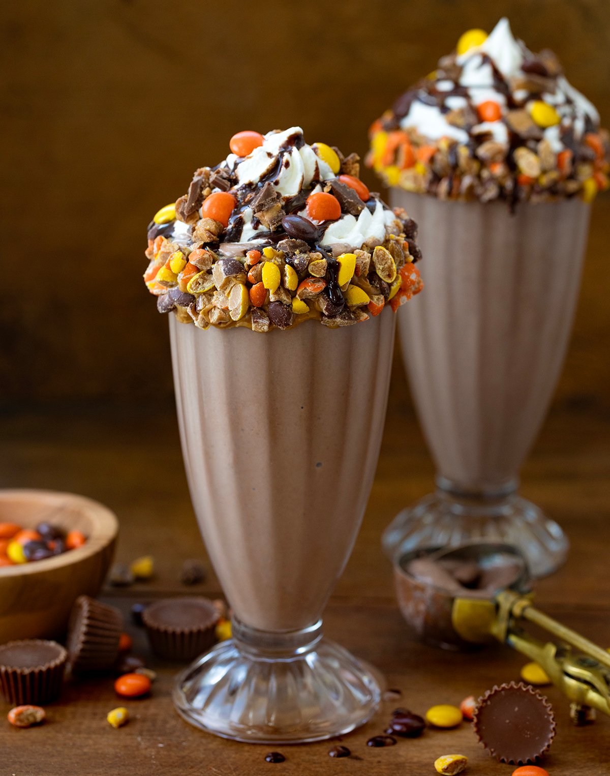 Two Ultimate Peanut Butter Chocolate Milkshakes on a wooden table.