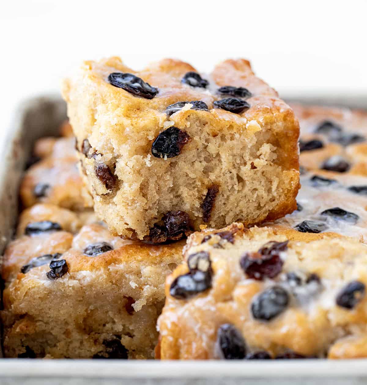 These Cinnamon Raisin Butter Swim Biscuits are a delicious variation of my popular Butter Swim Biscuits, adding the popular flavors of cinnamon and raisins to the mix. Like the original Butter Swim Biscuits, theyโre incredibly soft, fluffy, and filled with rich, buttery goodness, but with an extra layer of texture and sweetness. One Cinnamon Raisin Butter Swim Biscuit sitting on top of other biscuits in a pan close up.