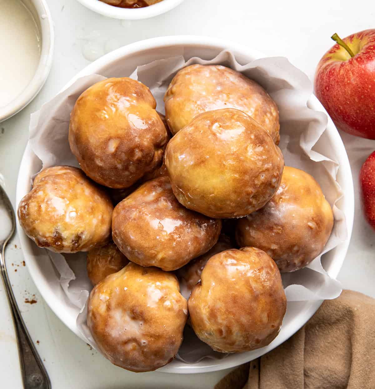 These easy Apple Fritter Bombs are made with biscuit dough, apple pie filling, and a sweet glaze, just like a mini apple fritter! White bowl filled with Apple Fritter Bombs on a white table from overhead.