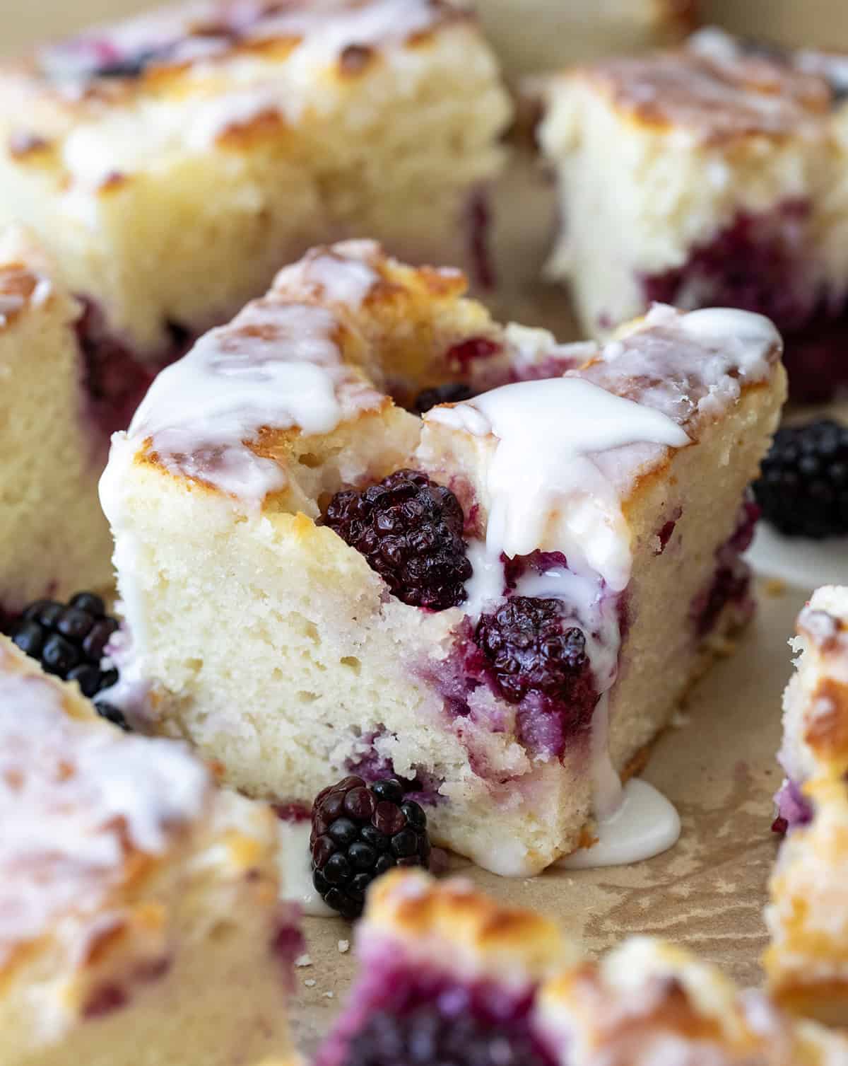 Blackberry Butter Swim Biscuits are buttery buttermilk biscuits filled with fresh blackberries and baked in melted butter, then topped with a simple, sweet glaze! Close up of a piece of Blackberry Butter Swim Biscuits with glaze dripping down the side.