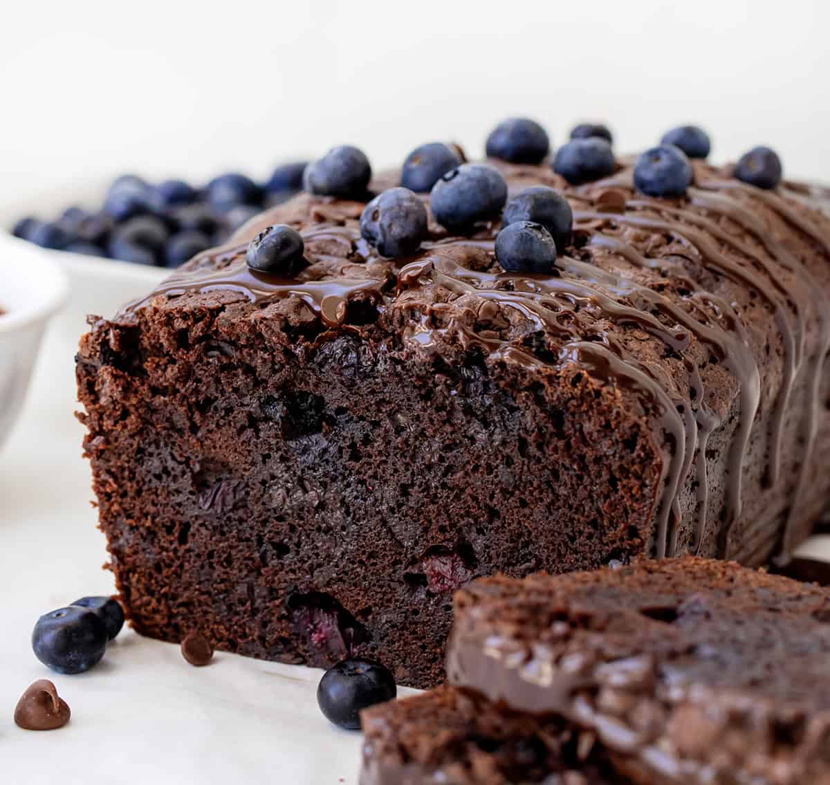Blueberry Brownie Bread is a rich, fudgy chocolate dessert loaf packed with juicy blueberries and chocolate chips. It’s the perfect mix of a brownie and a quick bread, moist, dense, and full of flavor in every bite! Sliced into loaf of Blueberry Brownie Bread showing tender texture and surrounded by blueberries.