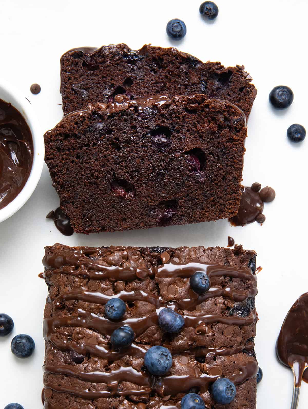 Blueberry Brownie Bread is a rich, fudgy chocolate dessert loaf packed with juicy blueberries and chocolate chips. It’s the perfect mix of a brownie and a quick bread, moist, dense, and full of flavor in every bite! Slices of Blueberry Brownie Bread laying flat on a white table from overhead.