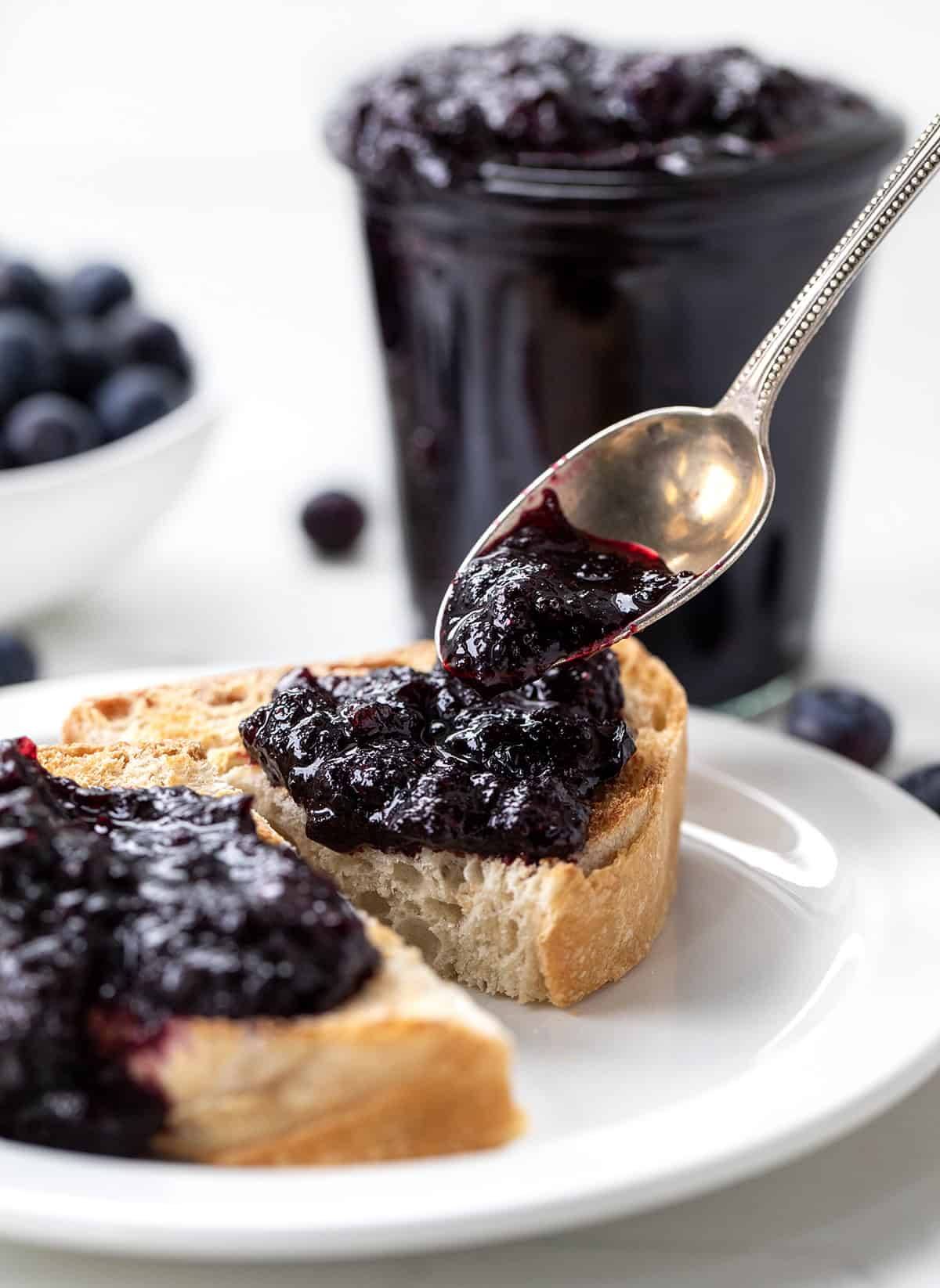 This Bourbon Blueberry Jam is thick, rich, and just sweet enough, with a warm depth of flavor from the bourbon... but does not taste like alcohol at all! Itโs made with pectin, so it sets up nicely and comes together quickly. If you have tried my blueberry jam without pectin (or bourbon) and loved it, I think youโll really enjoy this version, too! Spooning Bourbon Blueberry Jam over toast.