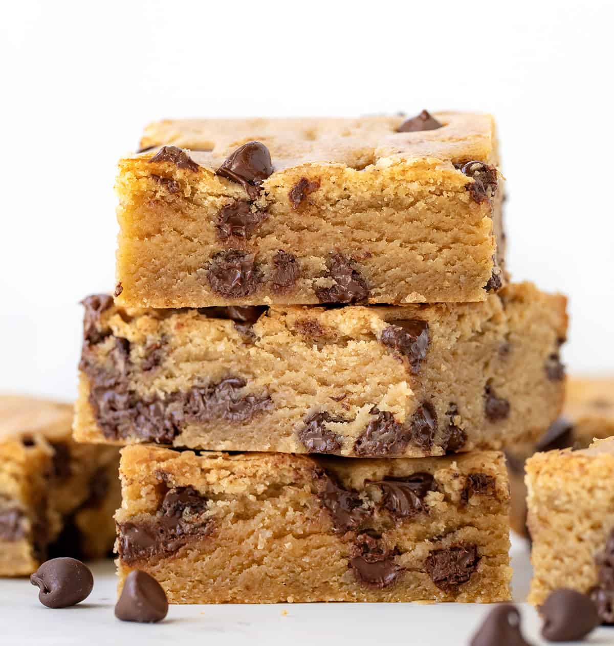 These Browned Butter Chocolate Chip Blondies are rich, chewy, and loaded with melty chocolate chips. If youโre looking for an easy dessert bar that tastes like a bakery treat, youโre in the right place! The browned butter adds a deep, nutty flavor that sets these chocolate chip blondies apart from anything youโve had before. Stack of Browned Butter Chocolate Chip Blondies on a white table.
