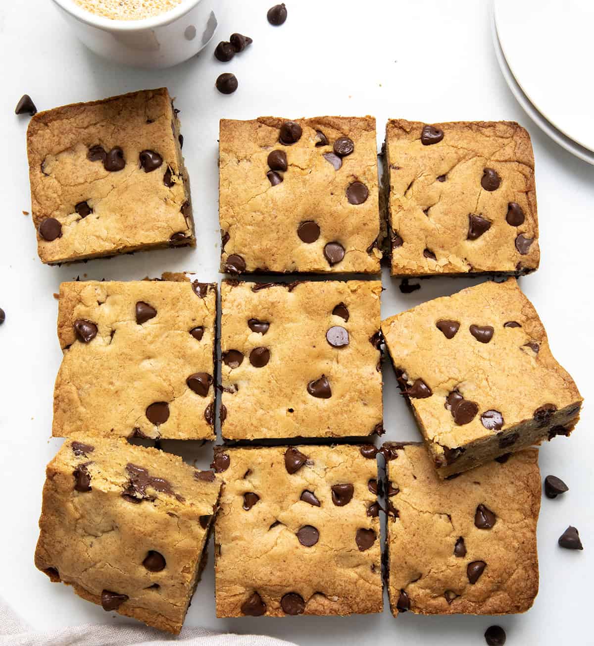 These Browned Butter Chocolate Chip Blondies are rich, chewy, and loaded with melty chocolate chips. If youโre looking for an easy dessert bar that tastes like a bakery treat, youโre in the right place! The browned butter adds a deep, nutty flavor that sets these chocolate chip blondies apart from anything youโve had before. Browned Butter Chocolate Chip Blondies cut into squares on a white table from overhead.