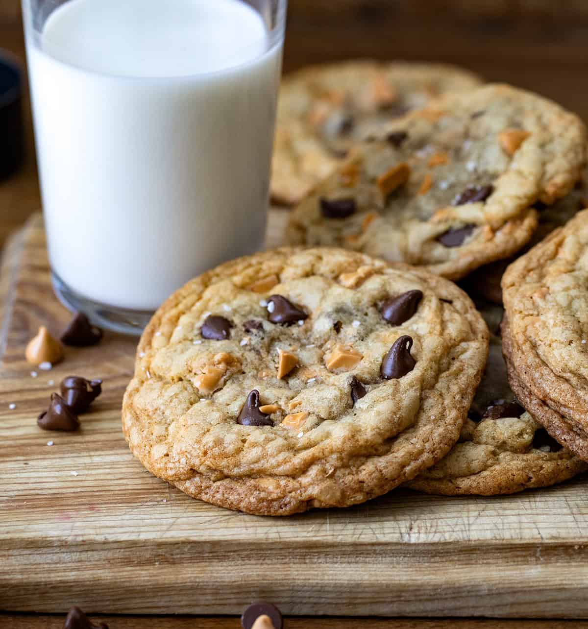 Butterscotch chocolate chip cookies are soft, chewy, and loaded with rich flavor from browned butter, semi-sweet chocolate, and sweet butterscotch chips! Close up of Butterscotch Chocolate Chip Cookies on a cutting board next to a glass of milk.