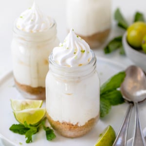Jars of Key Lime Cheesecake on a white platter on a white table with fresh key limes and mint.