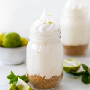 Jars of Key Lime Cheesecake on a white platter on a white table with fresh key limes and mint.