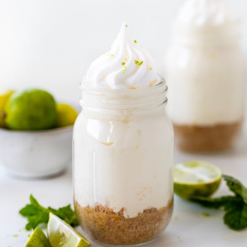 Jars of Key Lime Cheesecake on a white platter on a white table with fresh key limes and mint.
