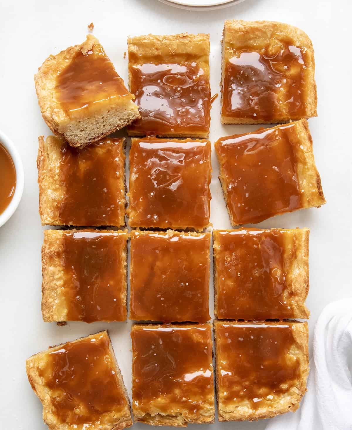 These Ooey Gooey Caramel Butter Bars are a sweet and salty dessert made with a cake mix crust, creamy filling, and caramel toppingโperfect for parties, holidays, or anytime you need an easy treat to feed a crowd! Ooey Gooey Caramel Butter Bars cut into pieces on a white table from overhead.