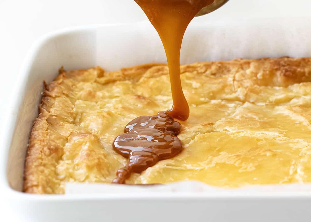 These Ooey Gooey Caramel Butter Bars are a sweet and salty dessert made with a cake mix crust, creamy filling, and caramel toppingโperfect for parties, holidays, or anytime you need an easy treat to feed a crowd! Drizzling caramel over Ooey Gooey Caramel Butter Bars.