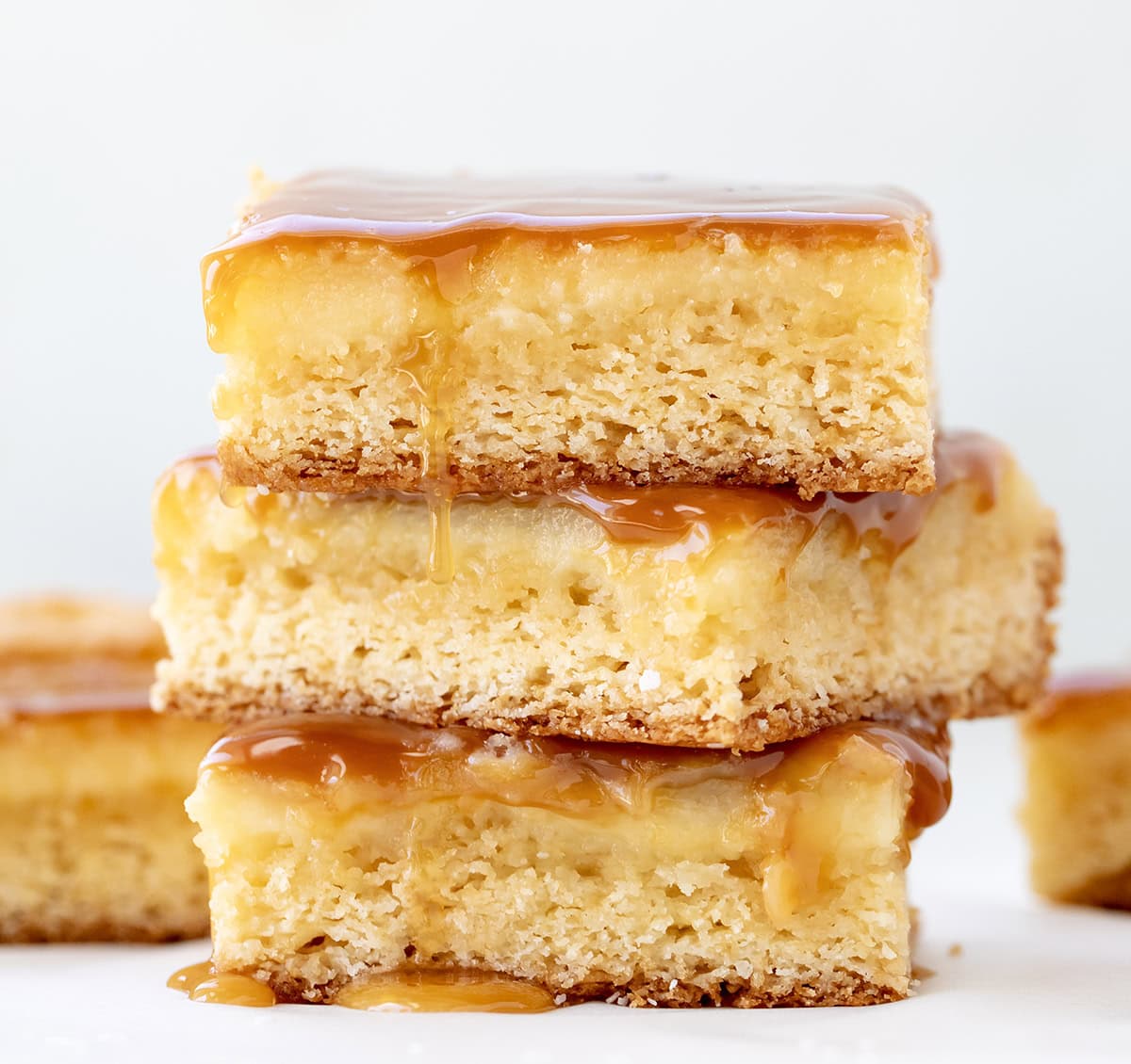 These Ooey Gooey Caramel Butter Bars are a sweet and salty dessert made with a cake mix crust, creamy filling, and caramel toppingโperfect for parties, holidays, or anytime you need an easy treat to feed a crowd! Stack of Ooey Gooey Caramel Butter Bars on a white table very close up.