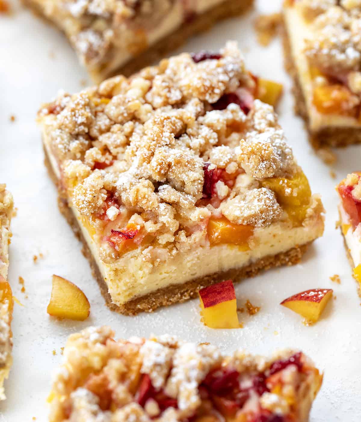 These Peach Cheesecake Bars have a buttery graham cracker crust, a creamy cheesecake layer, sweet diced peaches, and a cinnamon crumble topping. Every bite tastes like peach cobbler and cheesecake combined! Close up of cut into squares Peach Cobbler Cheesecake Bars.
