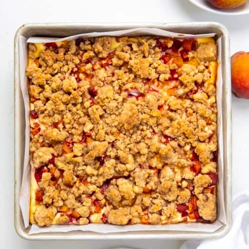 Pan of Peach Cobbler Cheesecake Bars on a white table from overhead.