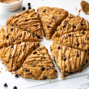 Peanut Butter Chocolate Chip Scones in a circle on a white table drizzled with peanut butter.