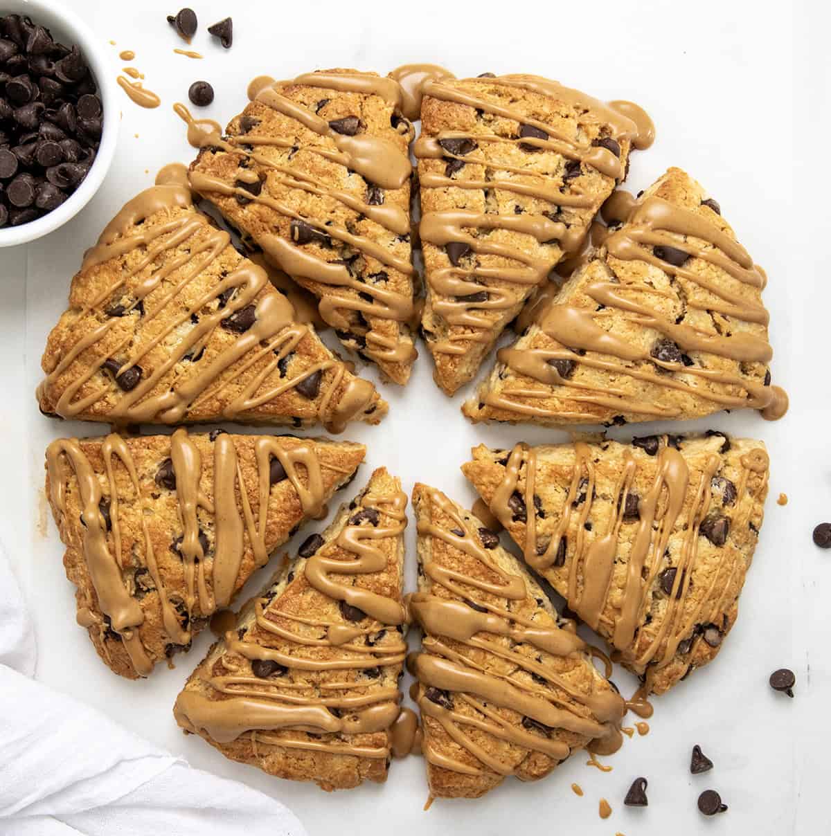 Peanut Butter Chocolate Chip Scones are my buttery, flaky chocolate chip scones taken to the next level with peanut butter mixed into the dough and drizzled on top. They are perfect for all my chocolate peanut butter lovers out there! Peanut Butter Chocolate Chip Scones in a circle on a white table rom overhead.
