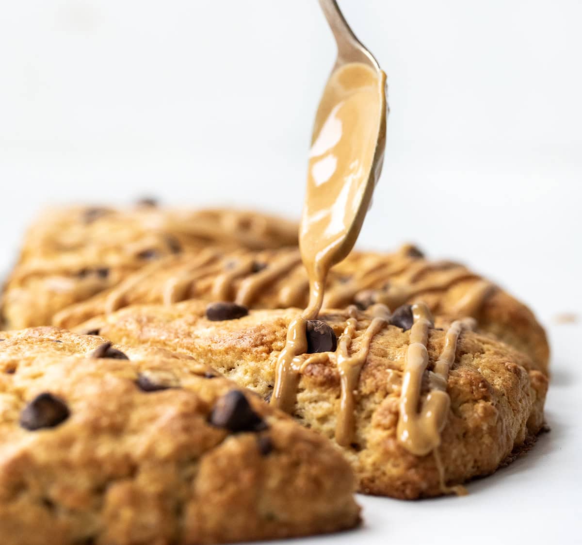 Peanut Butter Chocolate Chip Scones are my buttery, flaky chocolate chip scones taken to the next level with peanut butter mixed into the dough and drizzled on top. They are perfect for all my chocolate peanut butter lovers out there! Drizzling peanut butter over chocolate chip scones.