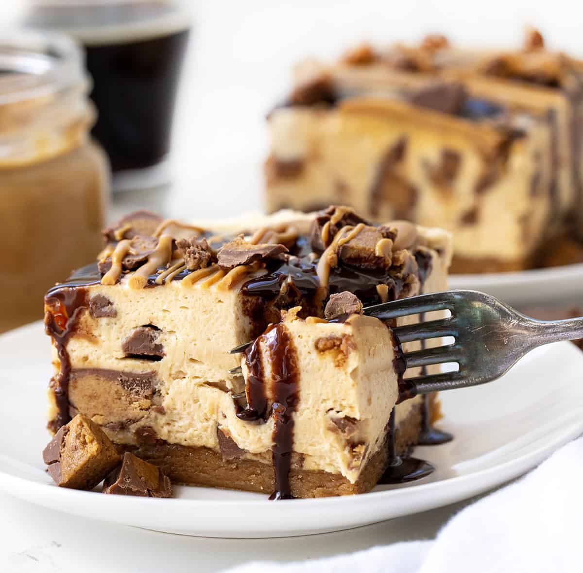 These Peanut Butter Cup Cheesecake Bars take my peanut butter cheesecake (which I absolutely love!) and turn it into easy-to-serve dessert bars. The bars start with a homemade easy peanut butter cookie crust, topped with a creamy peanut butter cheesecake filling loaded with chopped peanut butter cups. Fork taking a bite out of a piece of Peanut Butter Cup Cheesecake Bar.