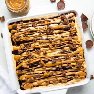 Peanut Butter Cup Cheesecake Bars on a white table with peanut butter cups from overhead.