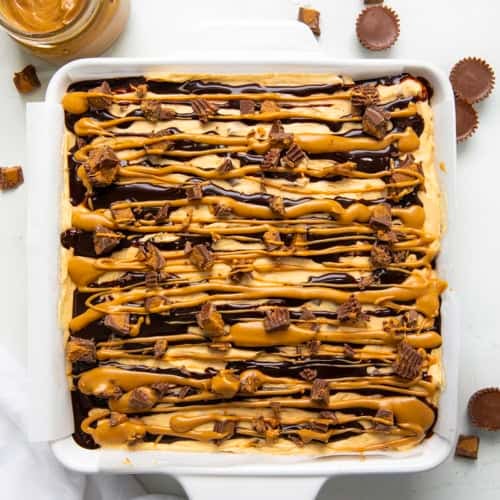 Peanut Butter Cup Cheesecake Bars on a white table with peanut butter cups from overhead.
