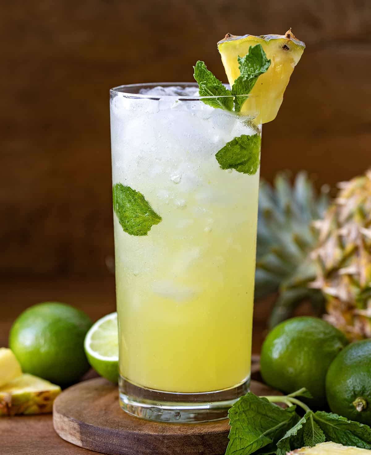 This Pineapple Mojito is a tropical twist on the classic, made with fresh mint, juicy pineapple, lime, light rum, and fizzy club soda for a crisp and refreshing drink. It’s the kind of cocktail you make when you want something that feels a little fancy but takes just minutes to throw together! One Pineapple Mojito on a wooden table surrounded by limes and pineapple.