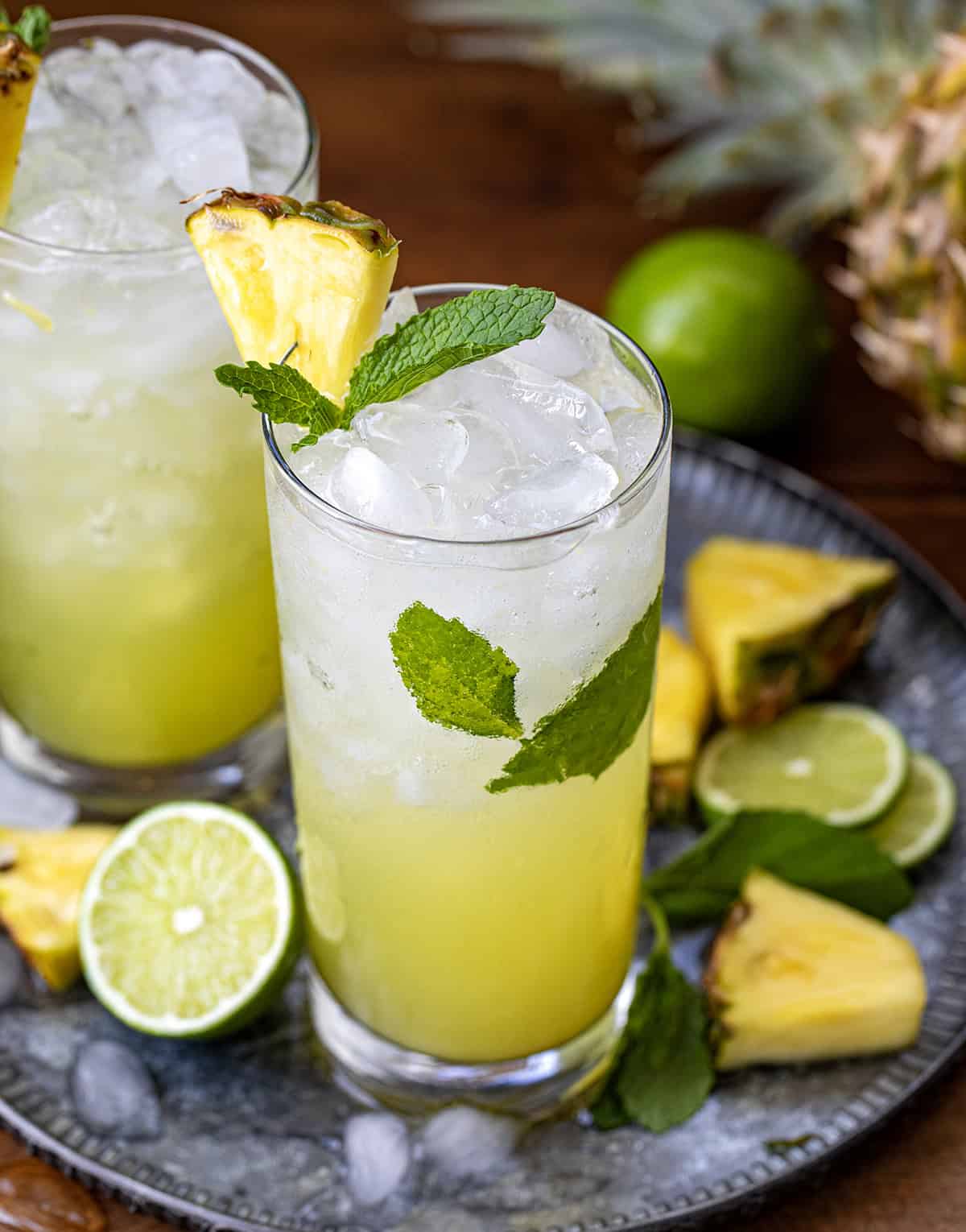This Pineapple Mojito is a tropical twist on the classic, made with fresh mint, juicy pineapple, lime, light rum, and fizzy club soda for a crisp and refreshing drink. It’s the kind of cocktail you make when you want something that feels a little fancy but takes just minutes to throw together! Looking down at Pineapple Mojito's on a tray with fresh lime and pineapple.
