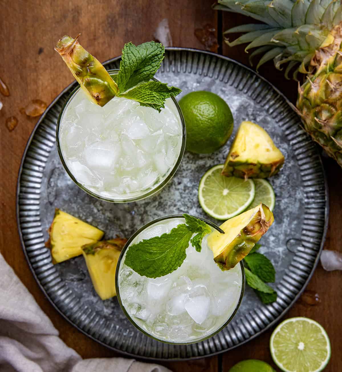 This Pineapple Mojito is a tropical twist on the classic, made with fresh mint, juicy pineapple, lime, light rum, and fizzy club soda for a crisp and refreshing drink. It’s the kind of cocktail you make when you want something that feels a little fancy but takes just minutes to throw together! Looking down on the top of Pineapple Mojito's on a tray on a wooden table.