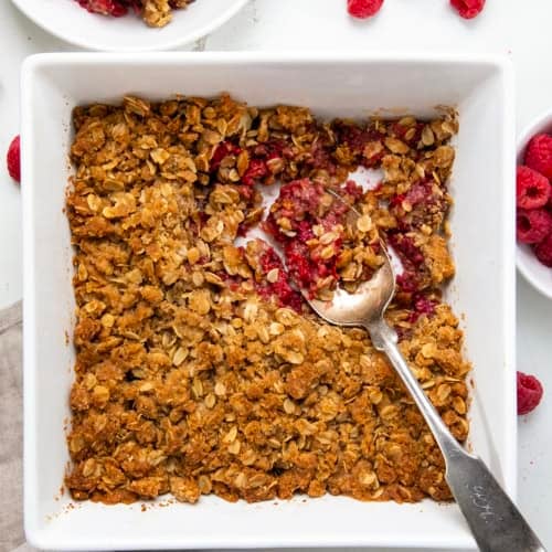 Pan of Raspberry Crisp with a spoon in it on a white table from overhead.