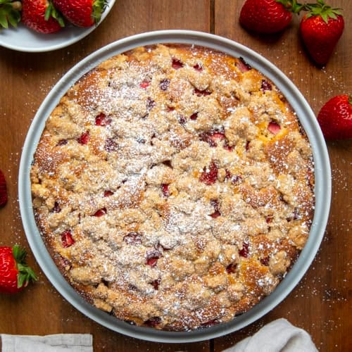 Whole Strawberries and Cream Coffee Cake on a white serving plate on a wooden table from overhead.