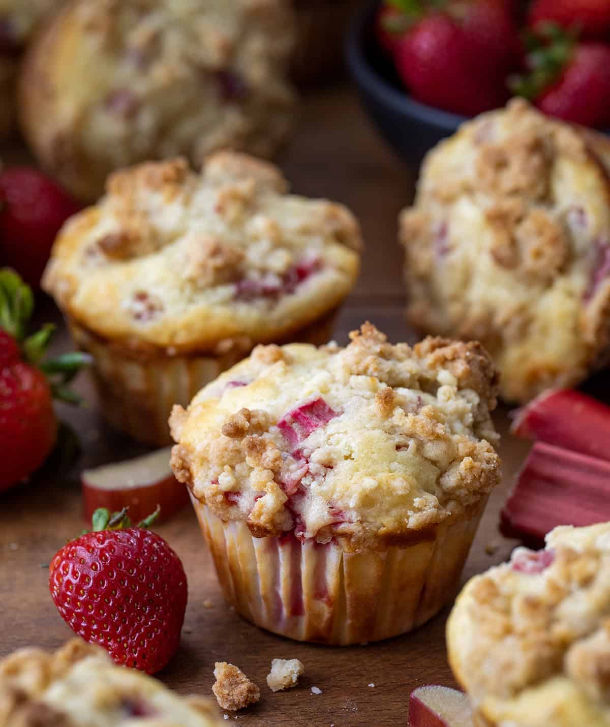 Strawberry Rhubarb Muffins are the perfect sweet-tart treat for spring and summer! Each soft, buttery muffin is packed with fresh strawberries and rhubarb, then topped with a golden crumb! Strawberry Rhubarb Muffins on a wooden table with fresh strawberries and rhubarbs.